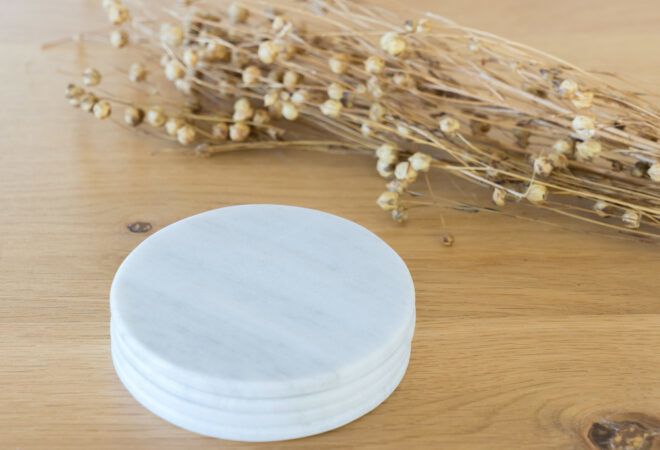 A stack of white coasters next to a bundle of dried flowers.