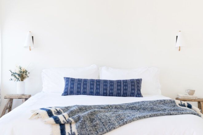 A white bed with a long blue pillow and blue blanket.
