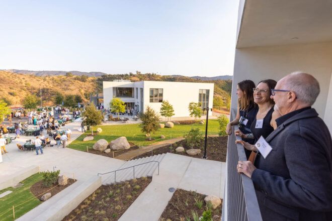 On the right, people looking off a balcony to a green campus courtyard to the left.