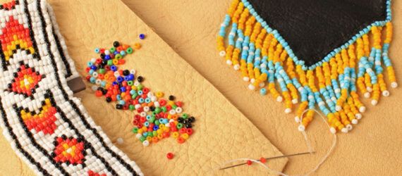 A threaded needle and beads scattered around two pieces of beaded art.