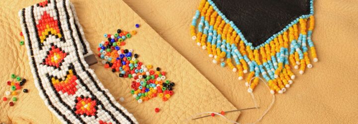 A threaded needle and beads scattered around two pieces of beaded art.