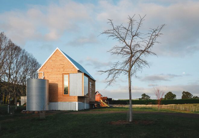 A green yard with a simple wood house with an attached steel water tank.