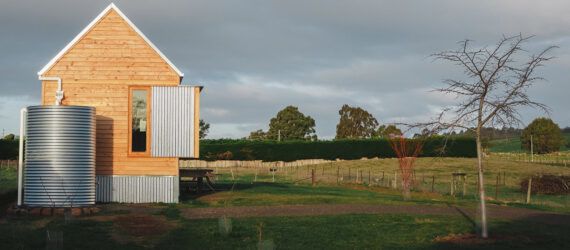 A green yard with a simple wood house with an attached steel water tank.