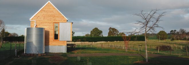 A green yard with a simple wood house with an attached steel water tank.