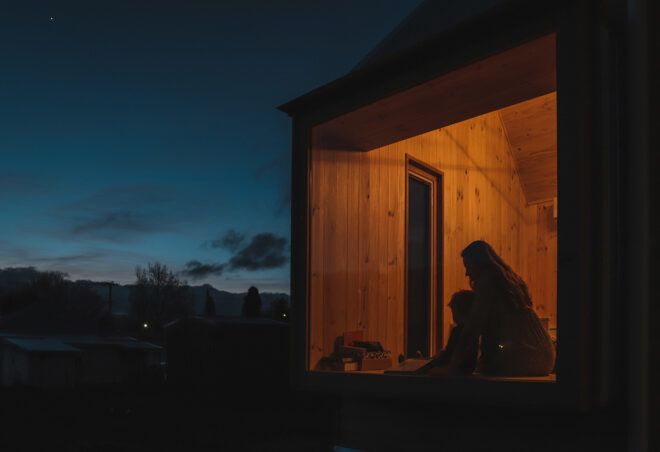 The shadows of a parent and child inside a lit-up home at night.