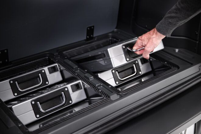 A hand pulling a metal case out of a pile of four metal cases.