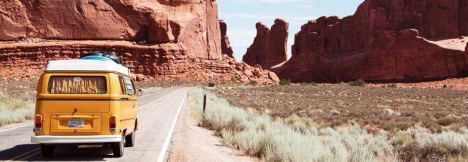 A yellow van driving down a desert road.