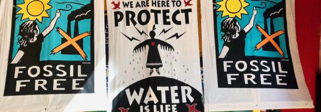 Protest signs reading "We are here to protect. Water is life." and "Fossil free."