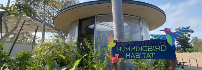 The exterior of a zoo building with a blue sign reading "Hummingbird Habitat."