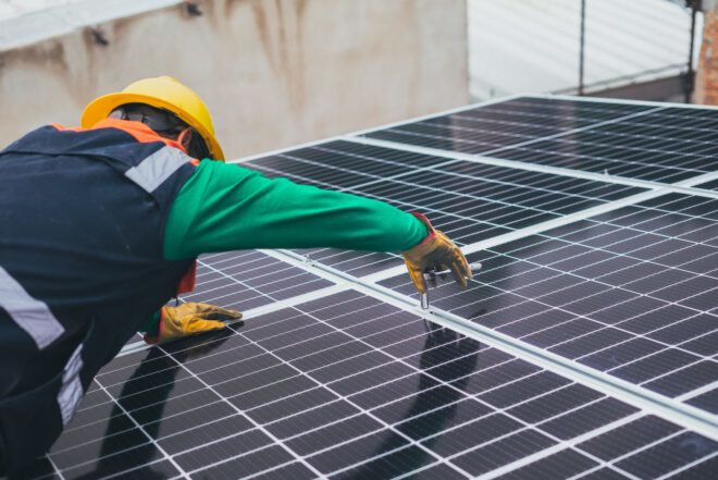 A person in construction clothes working on solar panels.