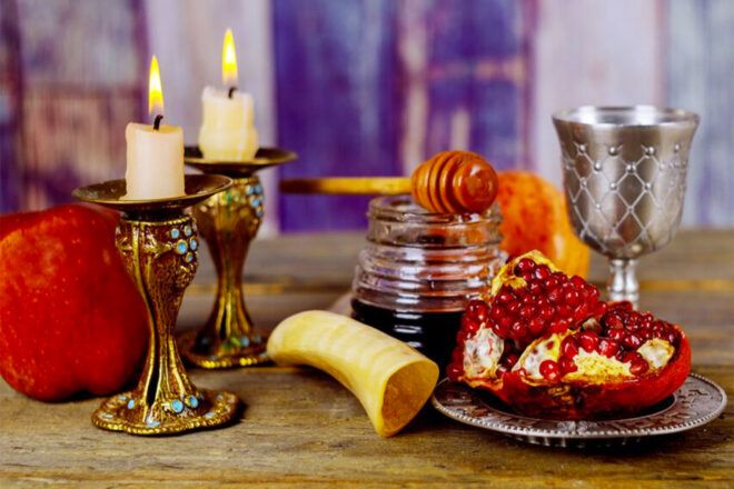 A spread of Rosh Hashanah decor, including candles, a horn, honey, a cup and pomegranates.