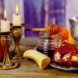 A spread of Rosh Hashanah decor, including candles, a horn, honey, a cup and pomegranates.
