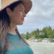 A person in a straw hat and blue shirt looking to the right at a sandy beach.