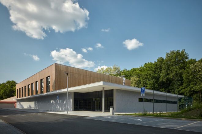 Building with a wood-covered volume popping out and forest in the background
