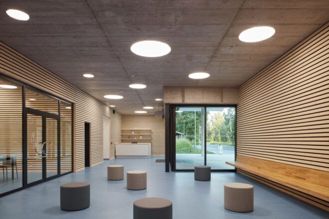 Wood-clad reception lobby with scattered seating poufs and a glass entry door