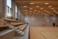 Seating tribune overlooking a court under a wood-clad ceiling with suspended lights