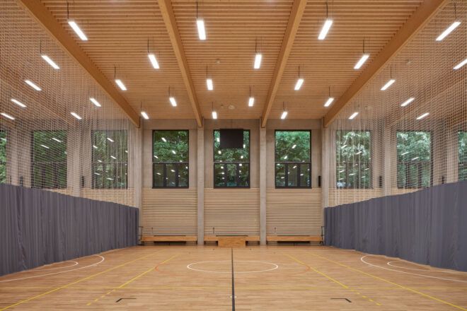 Court separated into three spaces with sports netting under a wood-clad ceiling with suspended lights