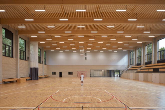 View of the court facing the entry lobby. Seating on the sides and a wood-clad ceiling with suspended lighting