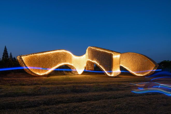 An abstract-shaped bamboo pavilion lit up in the evening.