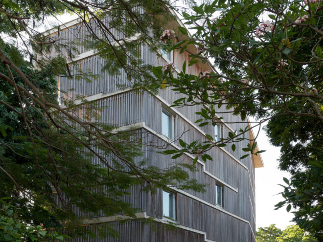 Side view of apartment block covered in wood slats shaded by trees