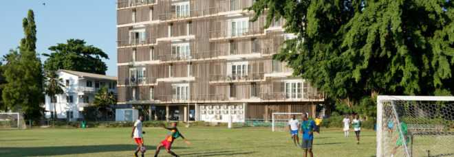 Players on soccer field with apartment building in the background