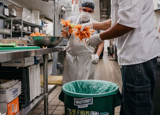 Two people in a kitchen putting items into a composting bin.