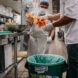 Two people in a kitchen putting items into a composting bin.