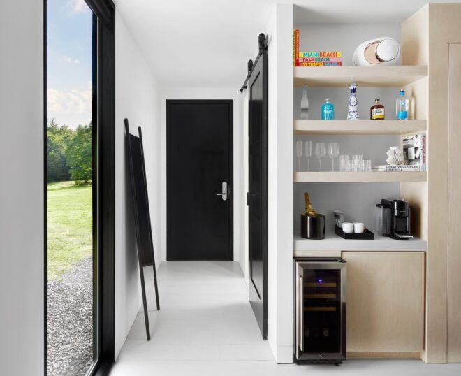 Interior white room opening into a hallway with shelves and floor length windows