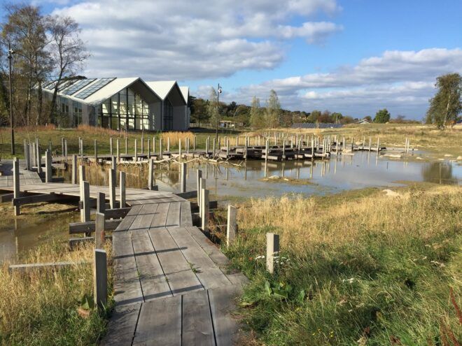Outside scenery of a building in a grassland area with a wooden platform bridge leading up to it