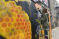 A woman painting on a step ladder a mural with honeycombs