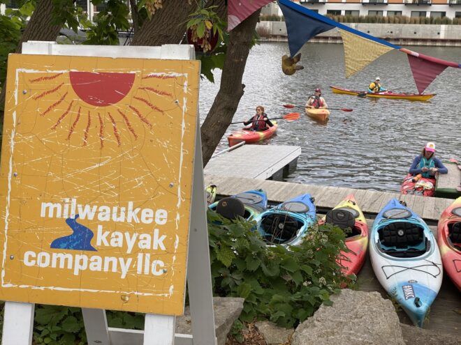 A stream with kayakers, with a sign "Milwaukee Kayak Company" in front of it