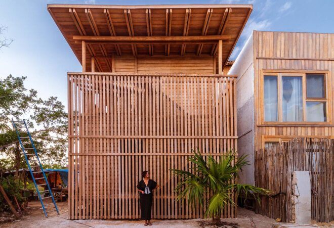 The exterior of a coconut palm wood home with a person standing out front.