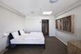 A white walled bedroom with a bed on the left with a painting facing across from it