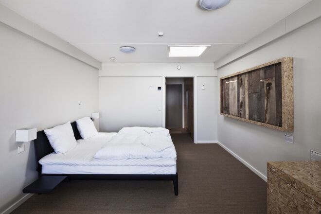 A white walled bedroom with a bed on the left with a painting facing across from it