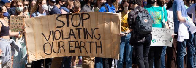 A line of protests holding a sign that says "Stop violating our earth."