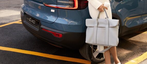A woman holding a bag leaning against a car