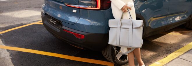 A woman holding a bag leaning against a car