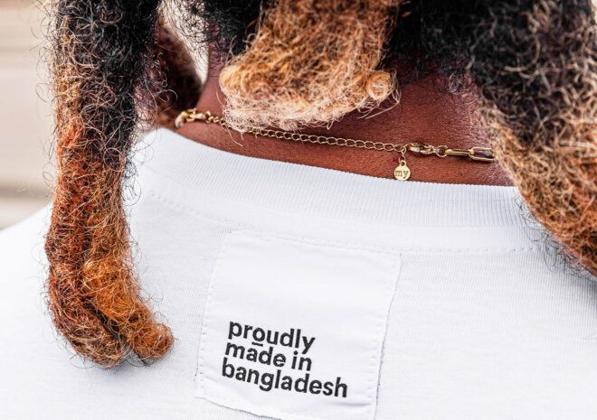 A person wearing a white t-shirt with a label reading "proudly made in bangladesh."