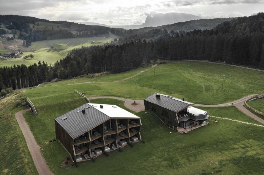 Two building sits in a field of grass against a hilly landscape