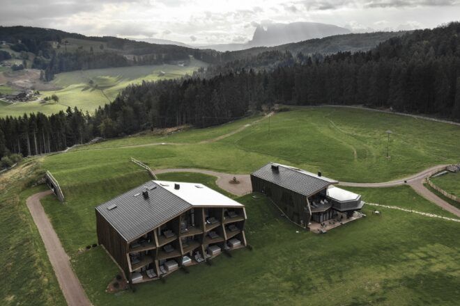 Two building sits in a field of grass against a hilly landscape