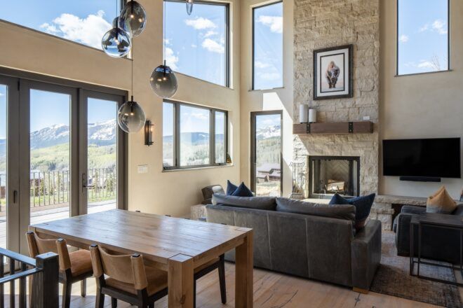 Living room with a table, sofa, fireplace and wall of windows