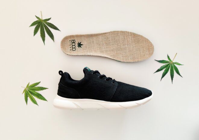 A black shoe with white insole laid on the side with an insole laid above it with marijuana leaves around it