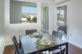 A dining room with four chairs around a square table and a white-walled apartment