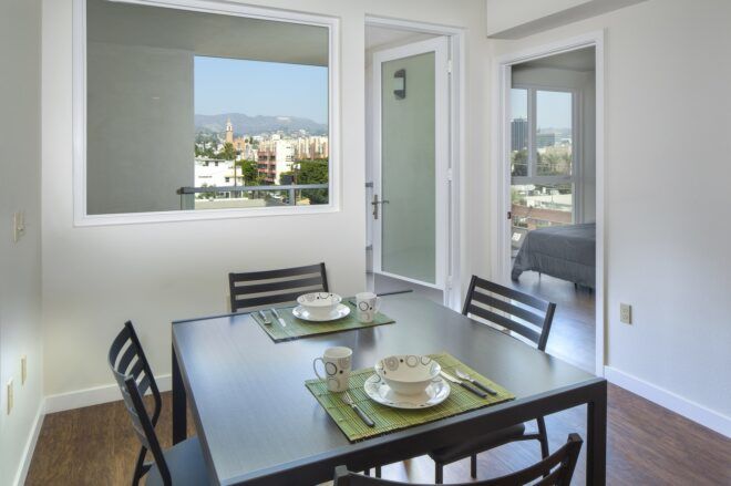 A dining room with four chairs around a square table and a white-walled apartment