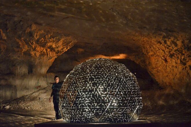 A man standing by a dome art structure in a cave