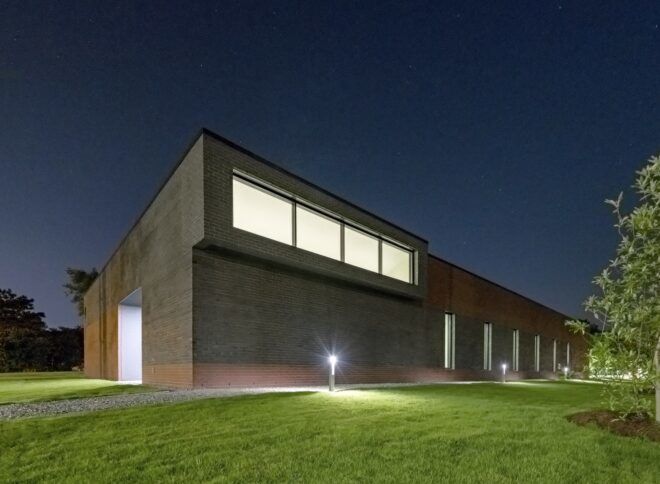 A building with a rectangular window at the top that has lights on during the night time