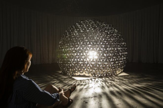A person watching a dome structure lit with light inside of it