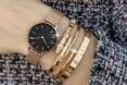 A wrist wearing a watch and several gold bracelets.