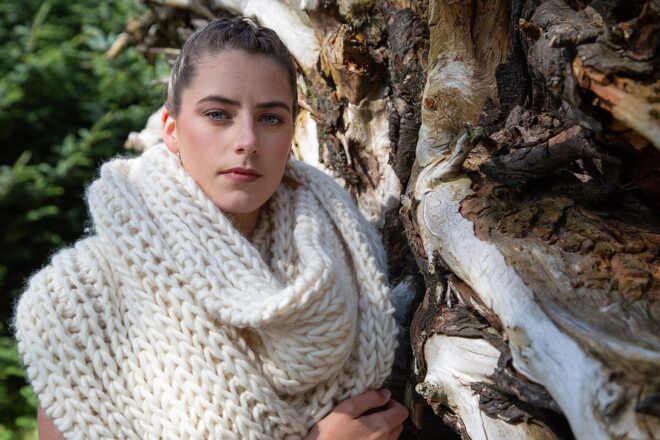 A woman leaning against a tree wearing a woolen scarf