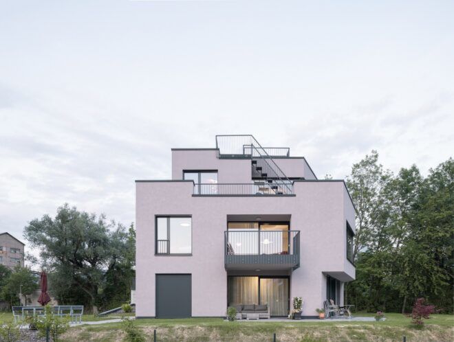 A pinkish white house sits against a landscape of trees and clouds